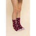 A pair of maroon fuzzy socks with a white heart pattern and scalloped edges, worn on a model's feet against a solid beige background.