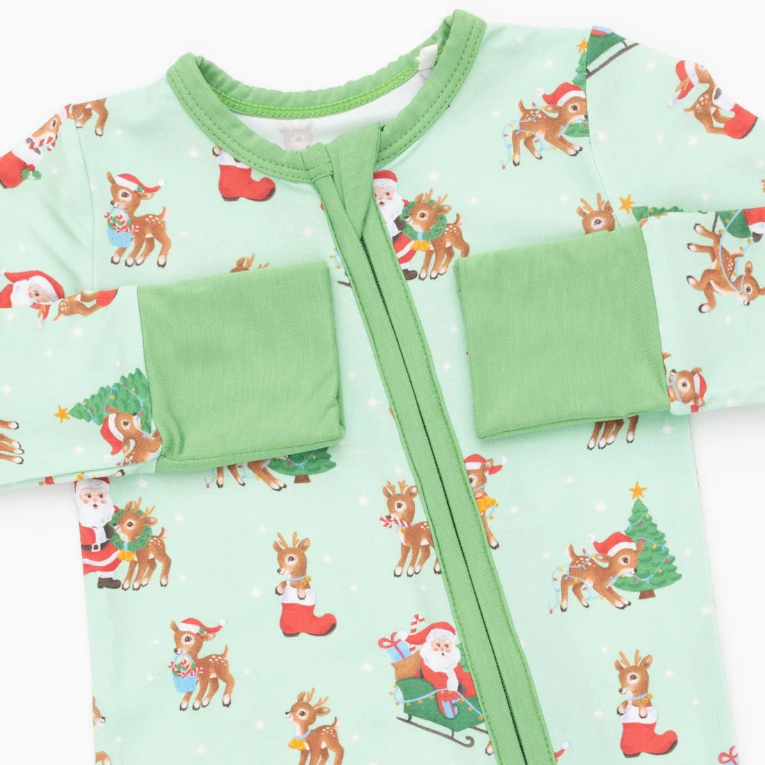 A baby zip-up sleeper in a light mint green color, decorated with a festive Christmas print featuring Santa Claus, reindeer, Christmas trees, and red stockings. The sleeper has two green pocket flaps on the chest and a green trim around the collar.