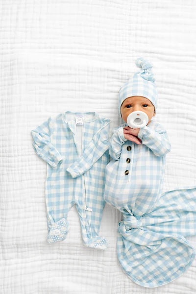 Newborn baby in blue checkered outfit and hat lying on a white textured surface