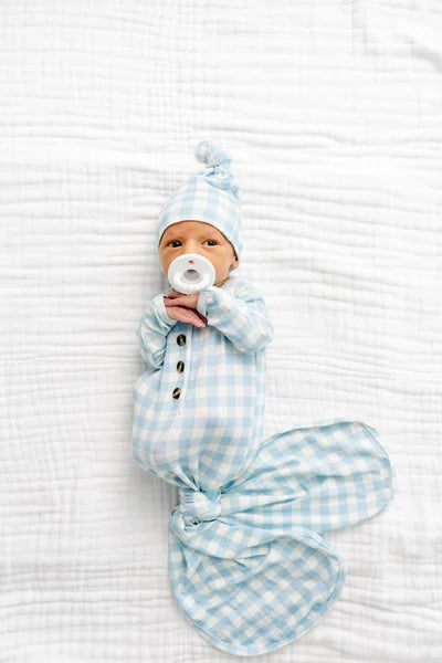 Newborn baby wrapped in a blue checkered swaddle with a matching hat on a white textured surface.