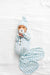 Newborn baby wrapped in a blue checkered swaddle with a matching hat on a white textured surface.