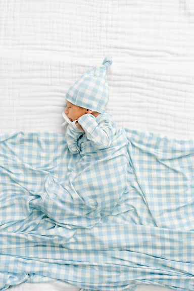 Baby wrapped in a blue checkered blanket with a matching hat on a white background
