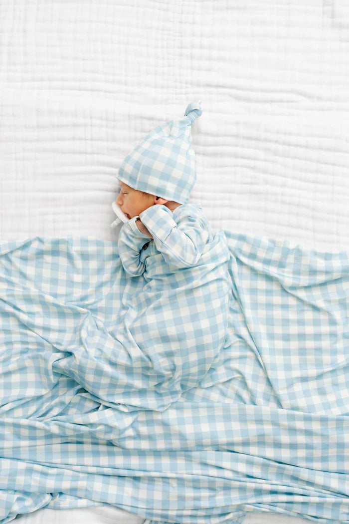 Baby wrapped in a blue checkered blanket with a matching hat on a white background