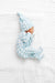 Baby in blue checkered outfit and hat lying on a white textured surface