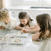 Three children sitting at a table with art supplies, engaged in a creative activity.