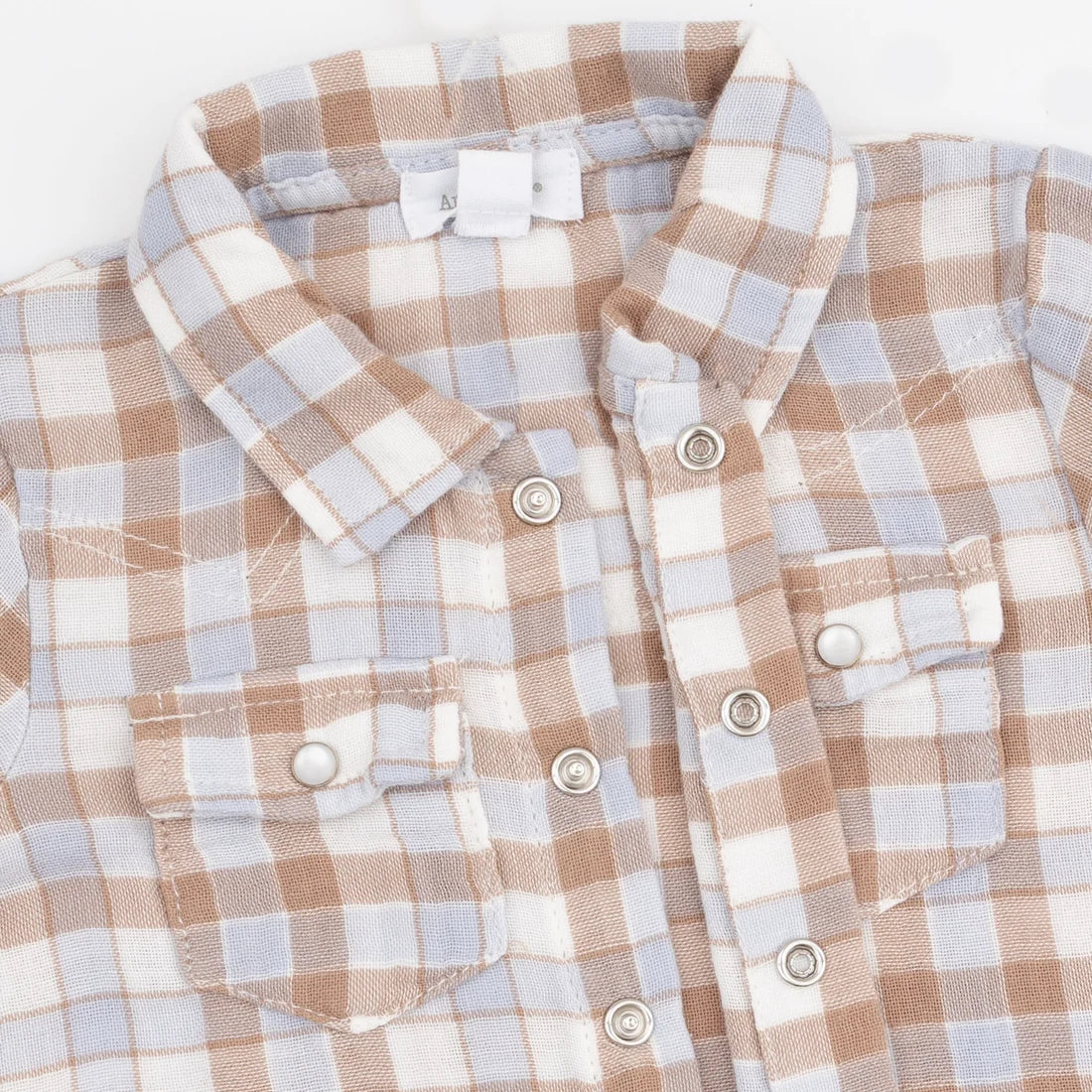 A close-up of a children's button-front shirt with a soft plaid pattern in beige, white, and light blue. The shirt features a pointed collar, two buttoned chest pockets, and silver-tone snap buttons.