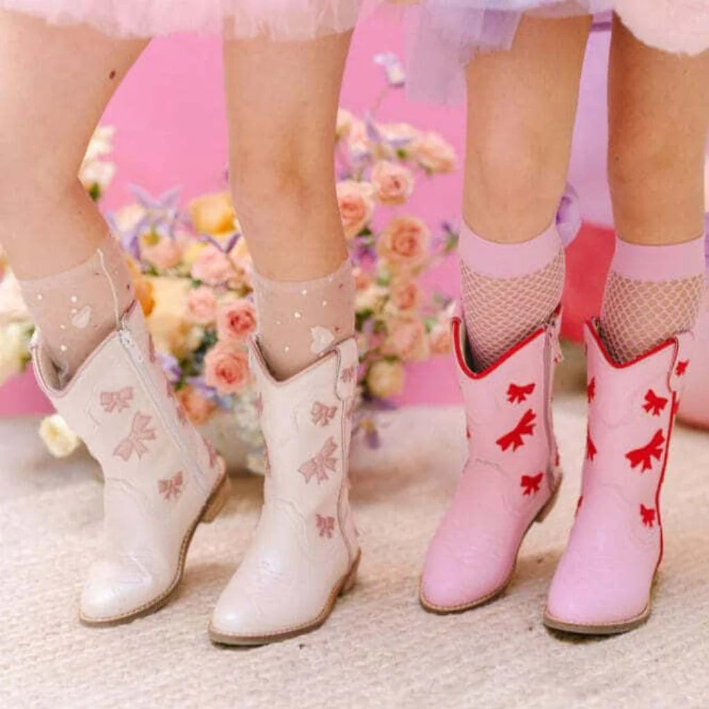 Children's white and pink cowboy boots with decorative elements on a floral background.
