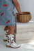 Child wearing a denim dress with cherry pattern and white boots with red cherries, standing next to a woven basket.