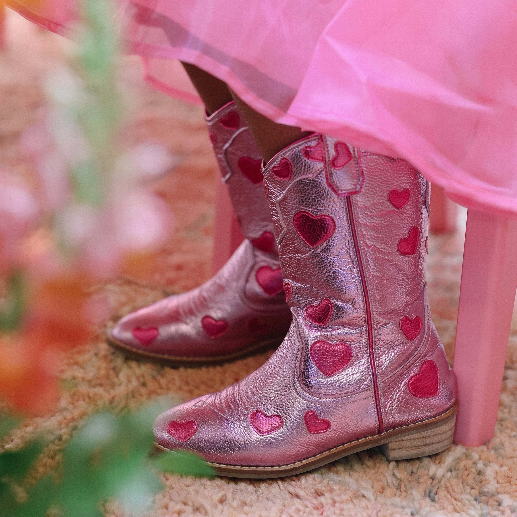 Pink cowboy boots with heart patterns worn by a child in a pink dress.