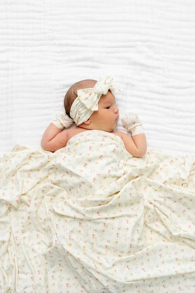 Newborn baby wrapped in a white blanket with a bow on a white background