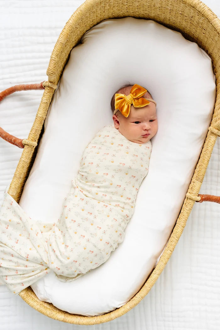 Newborn baby wrapped in a swaddle with a yellow bow in a wooden crib.