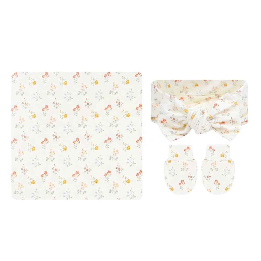A baby gift set featuring a square blanket, a knotted headband, and a pair of mittens, all in a soft cream color with a delicate multicolor floral pattern.