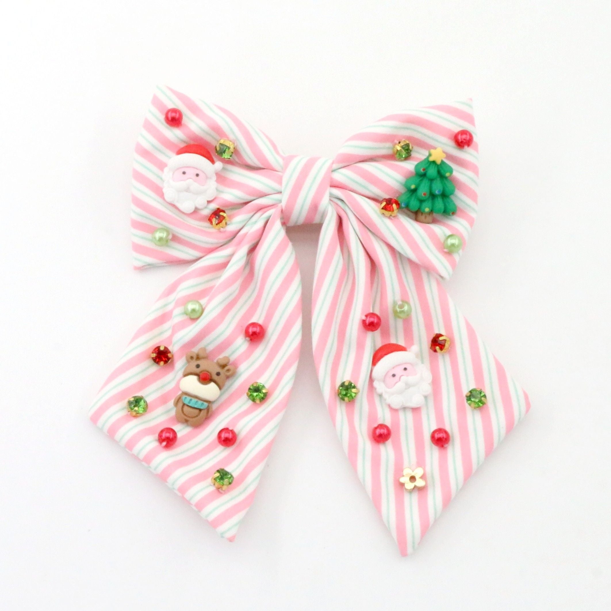 A pink and white striped fabric hair bow decorated with small Christmas-themed charms, including Santa Claus figures, a green Christmas tree, red and green beads, and a small gingerbread cookie charm, shown on a plain white background.