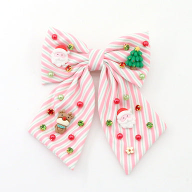 A pink and white striped fabric hair bow decorated with small Christmas-themed charms, including Santa Claus figures, a green Christmas tree, red and green beads, and a small gingerbread cookie charm, shown on a plain white background.