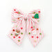 A pink and white striped fabric hair bow decorated with small Christmas-themed charms, including Santa Claus figures, a green Christmas tree, red and green beads, and a small gingerbread cookie charm, shown on a plain white background.