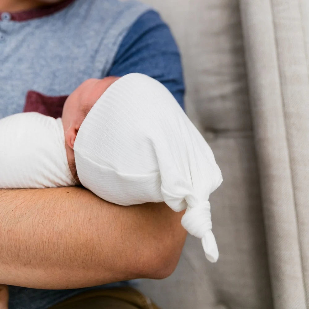 Person holding a baby wrapped in a white blanket on a couch.
