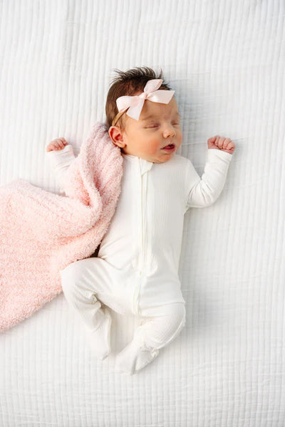 Newborn baby in a white onesie with a pink bow, lying on a white textured surface.