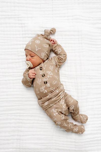 Newborn baby in a beige outfit with cowboy pattern on a white textured surface