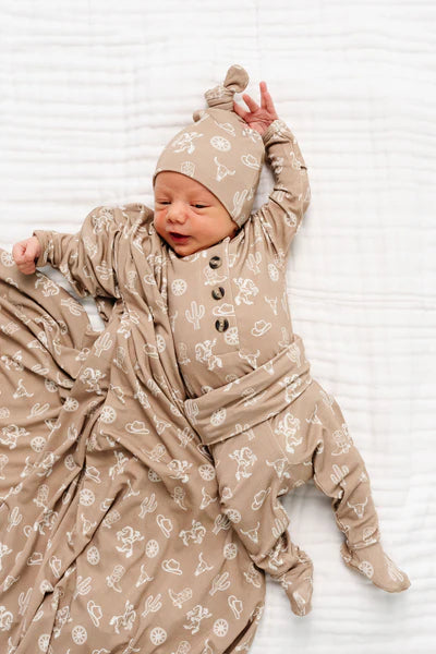 Newborn baby in a beige outfit with cowboy pattern on a white background