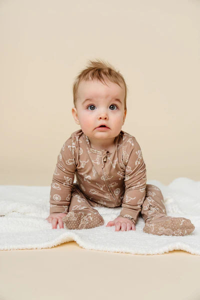 Baby wearing a brown onesie with a western pattern on a beige background