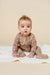 Baby wearing a brown onesie with a western pattern on a beige background