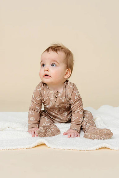 Baby wearing a brown western patterned outfit sitting on a white blanket against a beige background