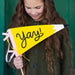 Child holding a yellow pennant with 'yay!' text against a green background