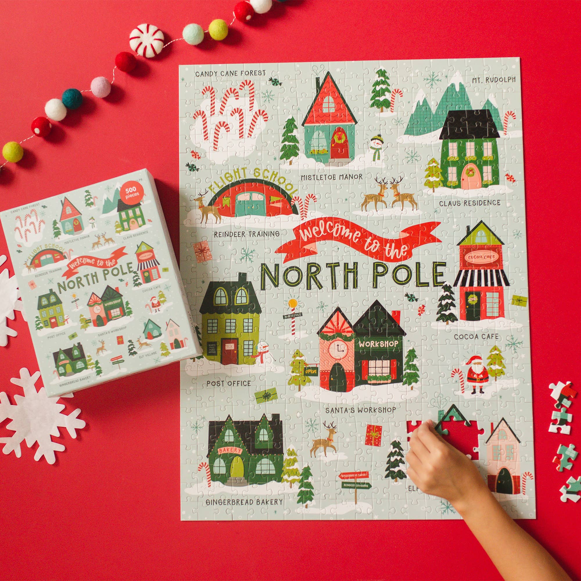 Pippi Post Welcome To The North Pole 500 piece jigsaw puzzle showing Santa village with candy cane forest workshop and festive homes as a hand assembles it