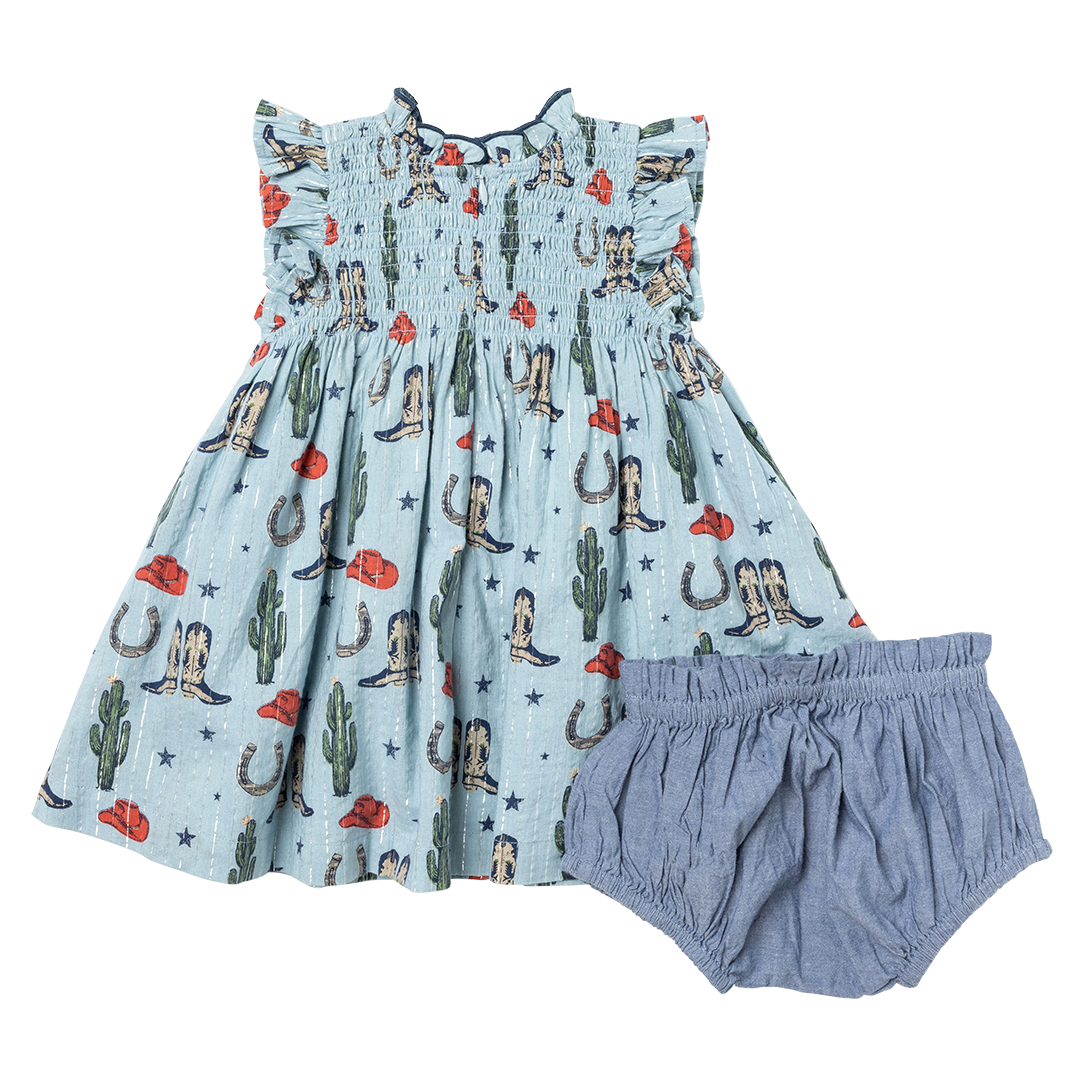 back of light blue sleeveless dress with smocking and rodeo print including boots, cactus and cowboy hats and chambray diaper cover