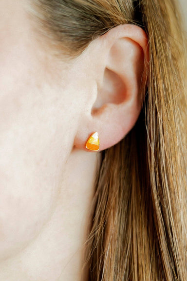 Close-up of an ear wearing a small candy corn earring with a blurred background