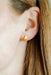 Close-up of an ear wearing a small candy corn earring with a blurred background