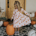 girl wearing pink long sleeved dress with orange, yellow and white candy corn print