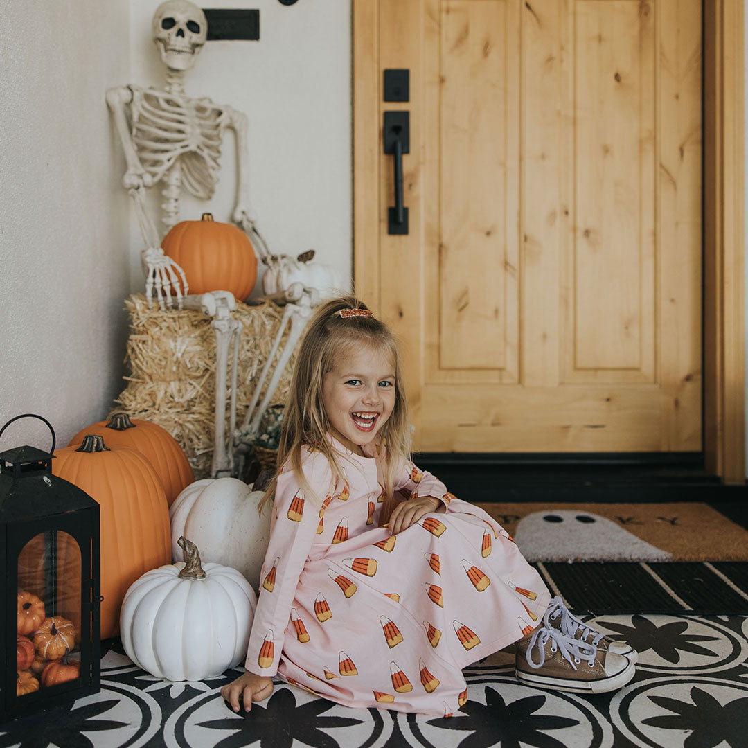 girl sitting wearing pink long sleeved dress with orange, yellow and white candy corn print