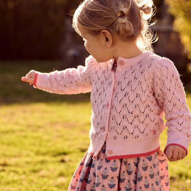 girl wearing light pink knit cardigan with glitter pink buttons and dark pink detail at the bottom of the sleeve waist