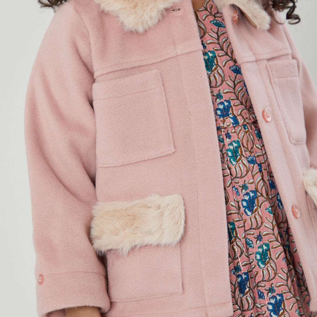 up close view of light pink pea coat with cream colored fur on pockets and collar while pink floral dress underneath