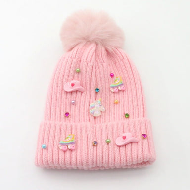 A light pink ribbed knit beanie hat with a fluffy pom-pom on top, decorated with pastel unicorn and roller skate embellishments and small rhinestone beads, shown on a plain white background.